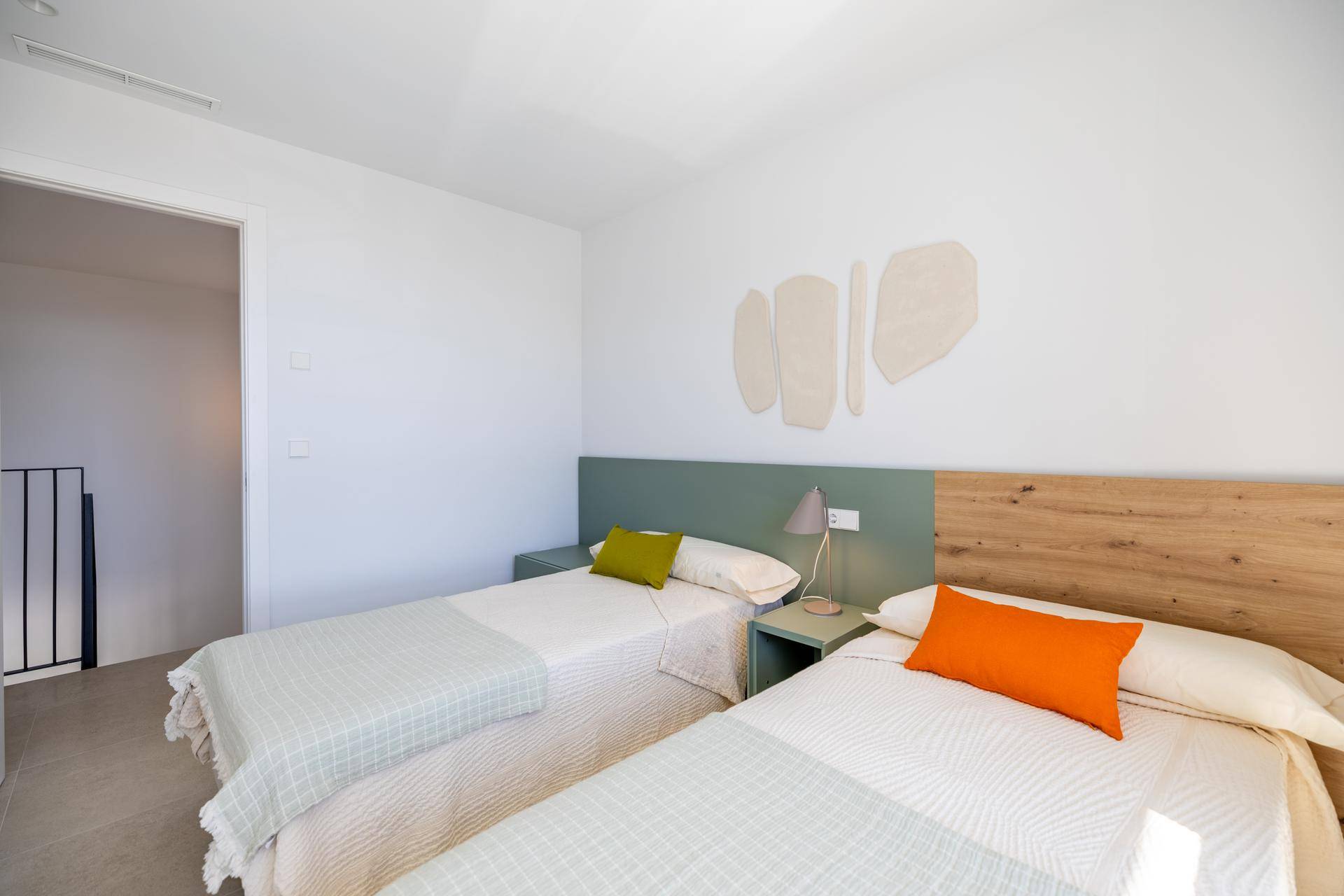 Gemütliches Schlafzimmer mit zwei Einzelbetten, schlichter Einrichtung und Zugang zum Flur.