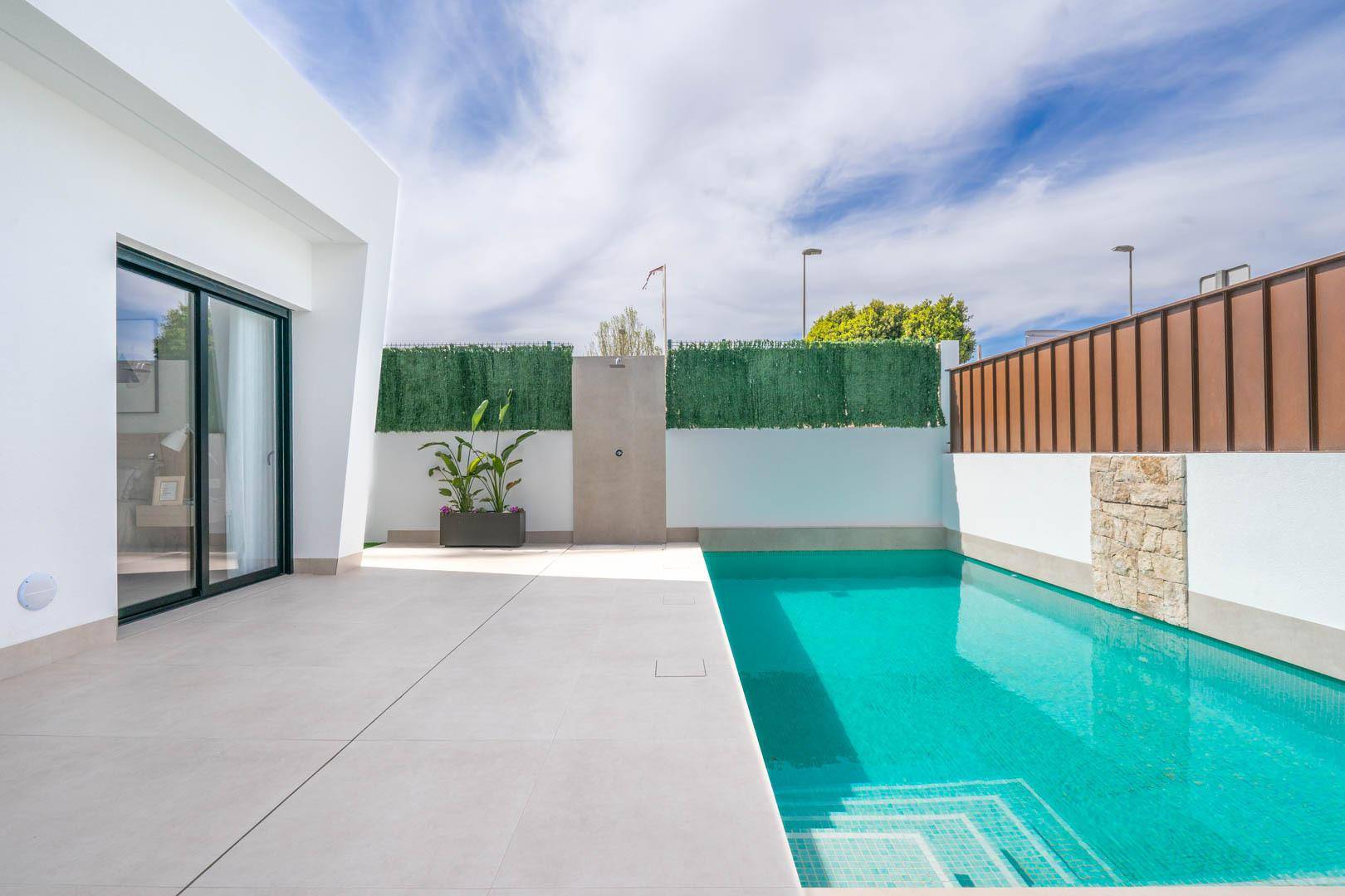 Sonnige Terrasse mit Pool und Außendusche, umgeben von einer grünen Hecke.