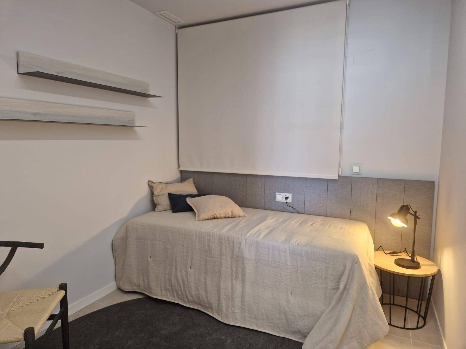 Gemütliches Schlafzimmer mit Einzelbett, Beistelltisch und Fenster mit modernem Rollo.