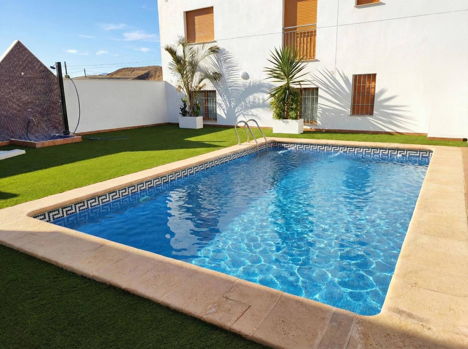 Rechteckiger Swimmingpool mit blauen Fliesen und Kunstrasen im privaten Gartenbereich.