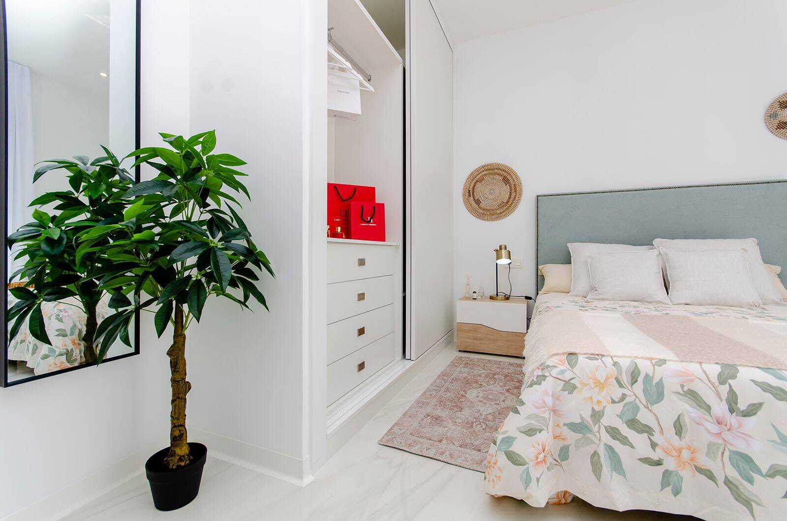 Modernes Schlafzimmer mit integriertem Kleiderschrank, Pflanze und hellem Fliesenboden.