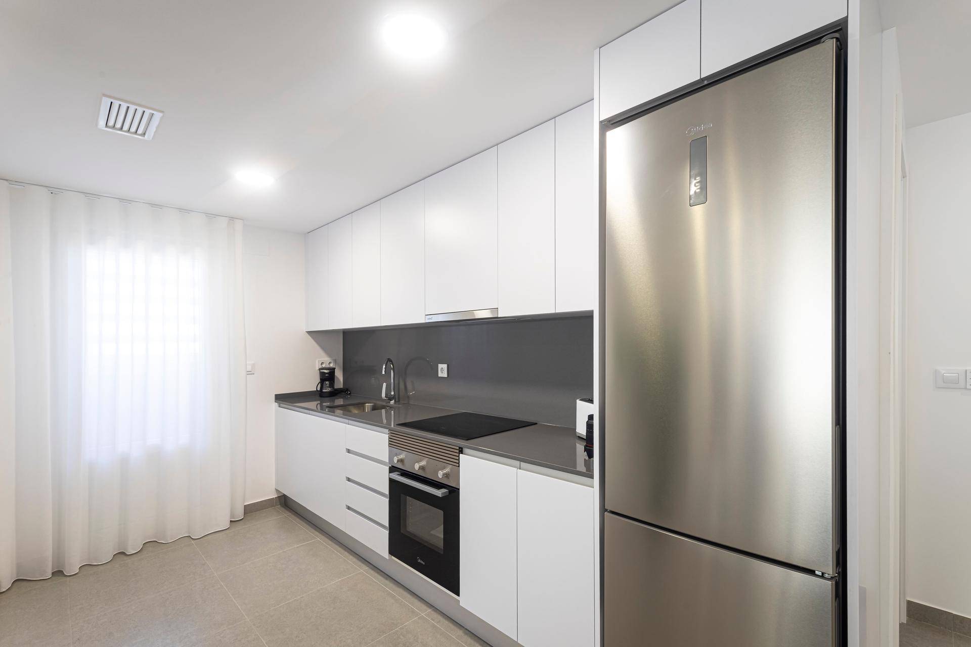 Helle Küche mit weißen Schränken, Edelstahlkühlschrank und Fliesenboden.