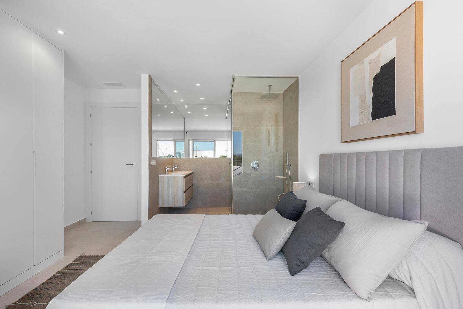 Schlafzimmer mit großem Bett, integriertem Kleiderschrank und offenem Badezimmerbereich mit Doppelwaschbecken.