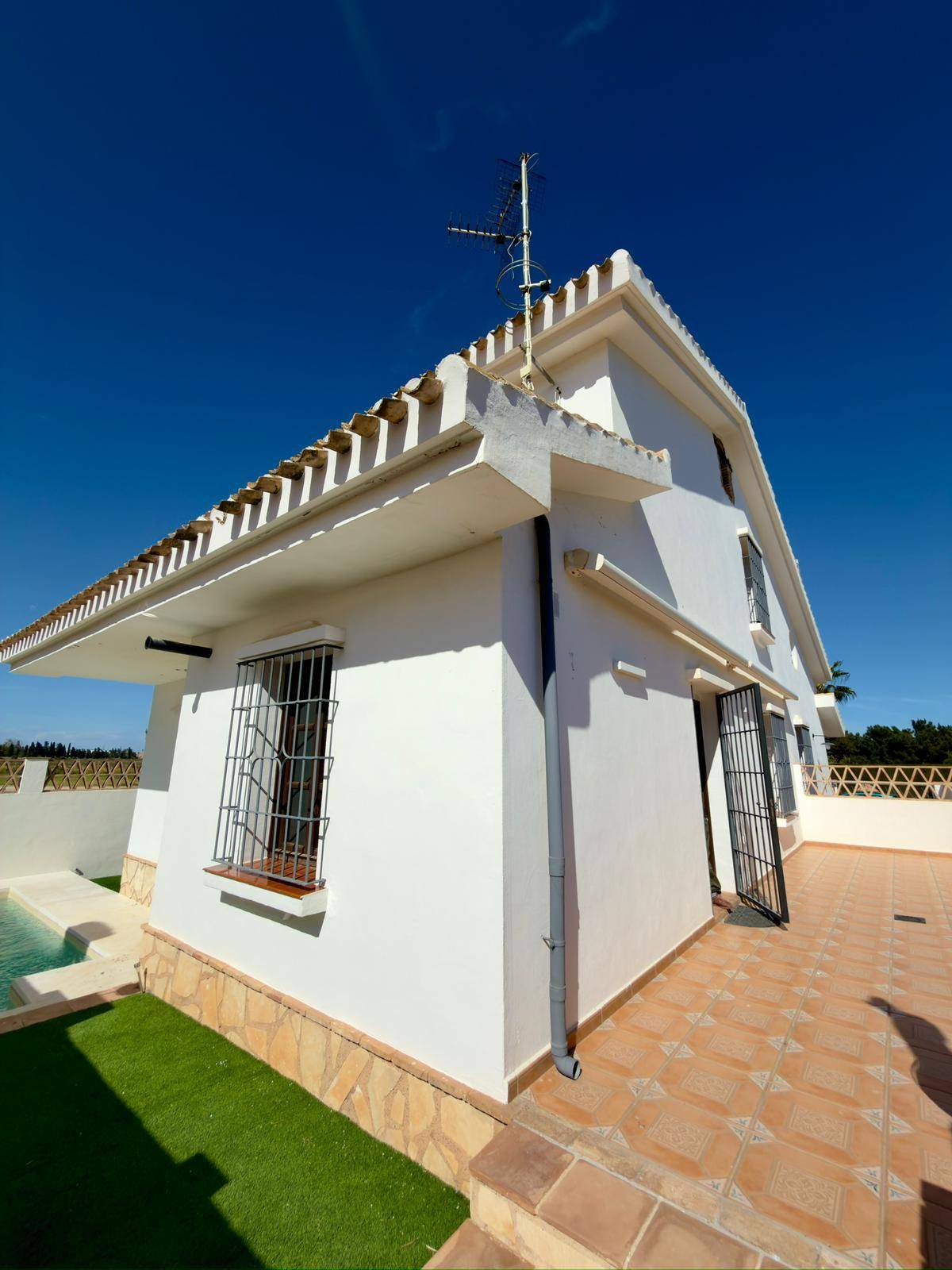 Seitenansicht der Villa mit Poolbereich und angrenzender gefliester Fläche.