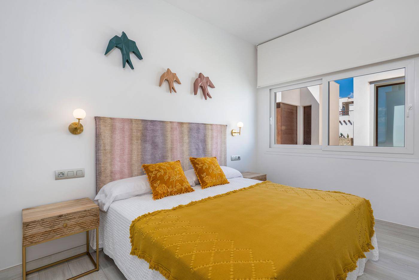 Schlafzimmer mit Doppelbett, farbenfrohem Kopfteil und modernem Nachttisch, hell und einladend.