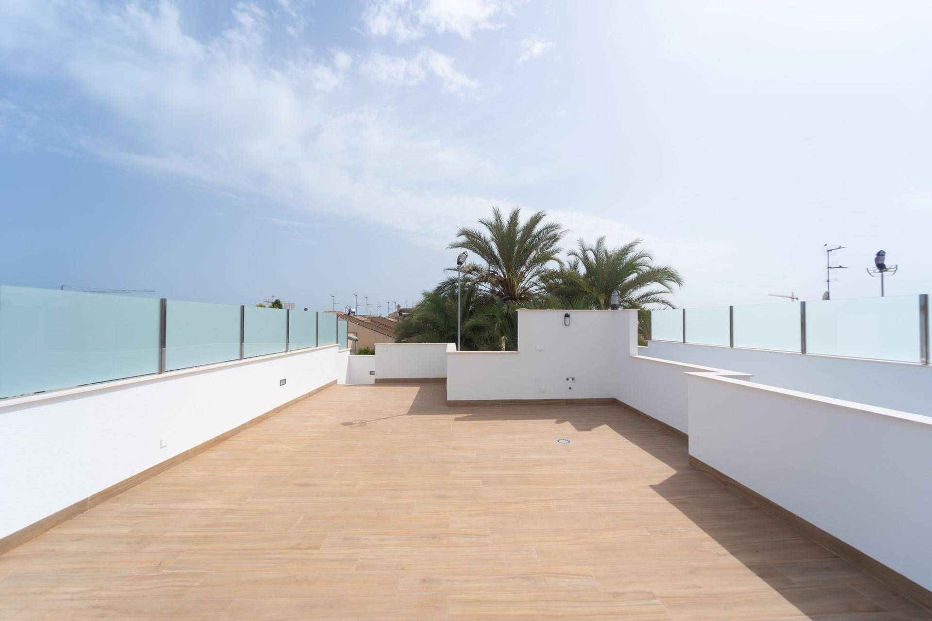 Geräumige Dachterrasse mit modernen Glasgeländern und weitem Blick auf Palmen und Umgebung.