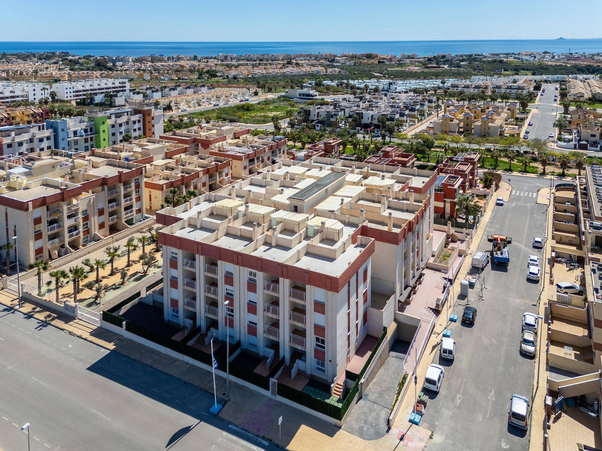 Luftaufnahme des Wohnkomplexes mit der Gebäudefassade, Straße und dem Meer in der Ferne.
