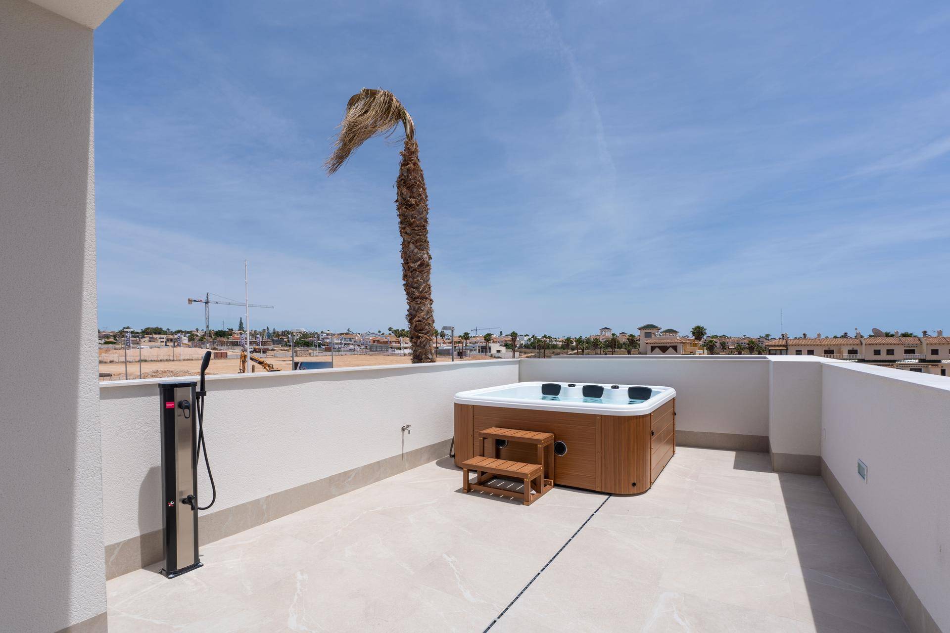 Sonniger Dachterrassenbereich mit Whirlpool, Außendusche und Blick auf die Stadt.