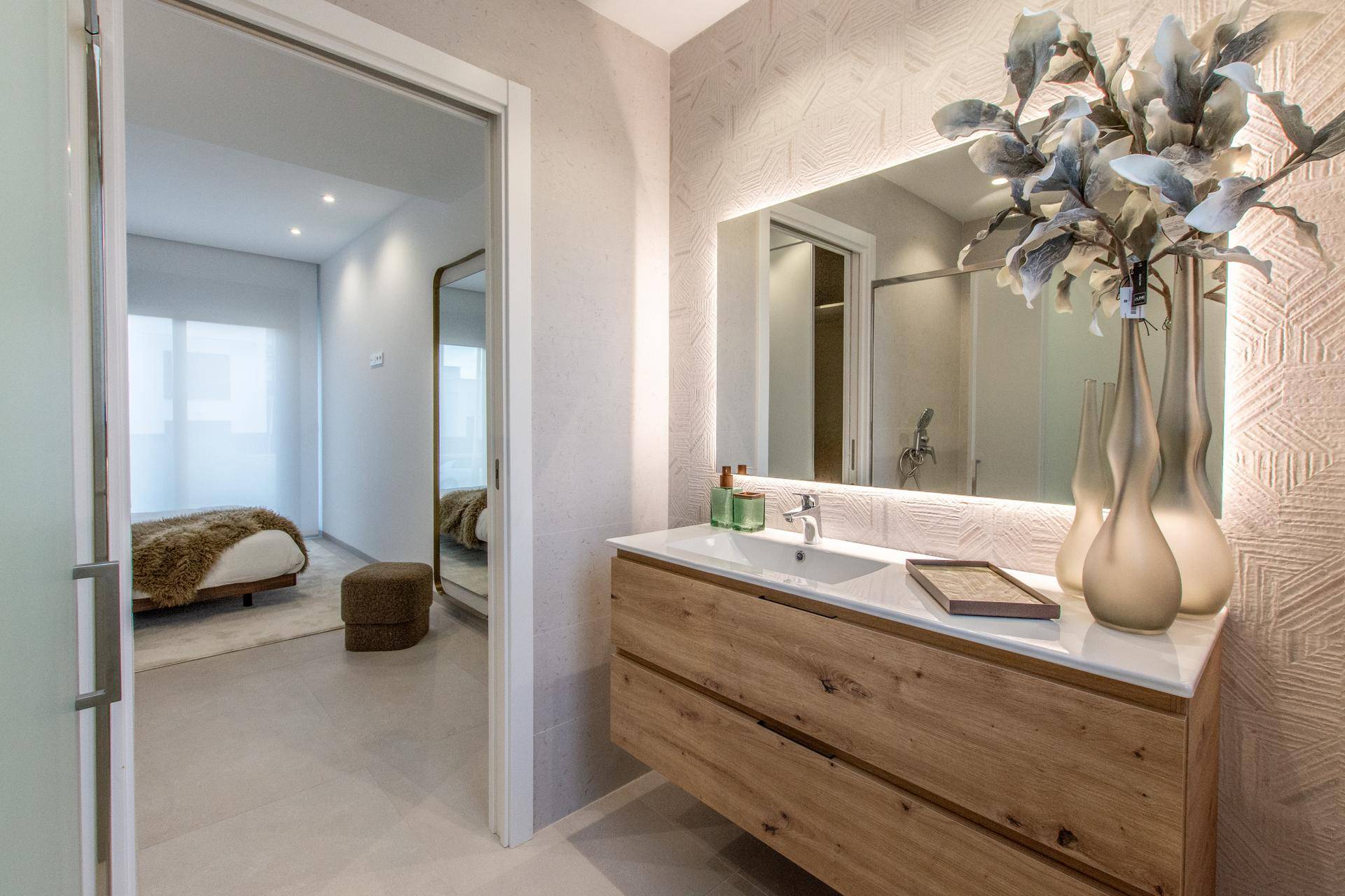 Elegantes Badezimmer mit Holzwaschtisch, beleuchtetem Spiegel und Zugang zum Schlafzimmer.