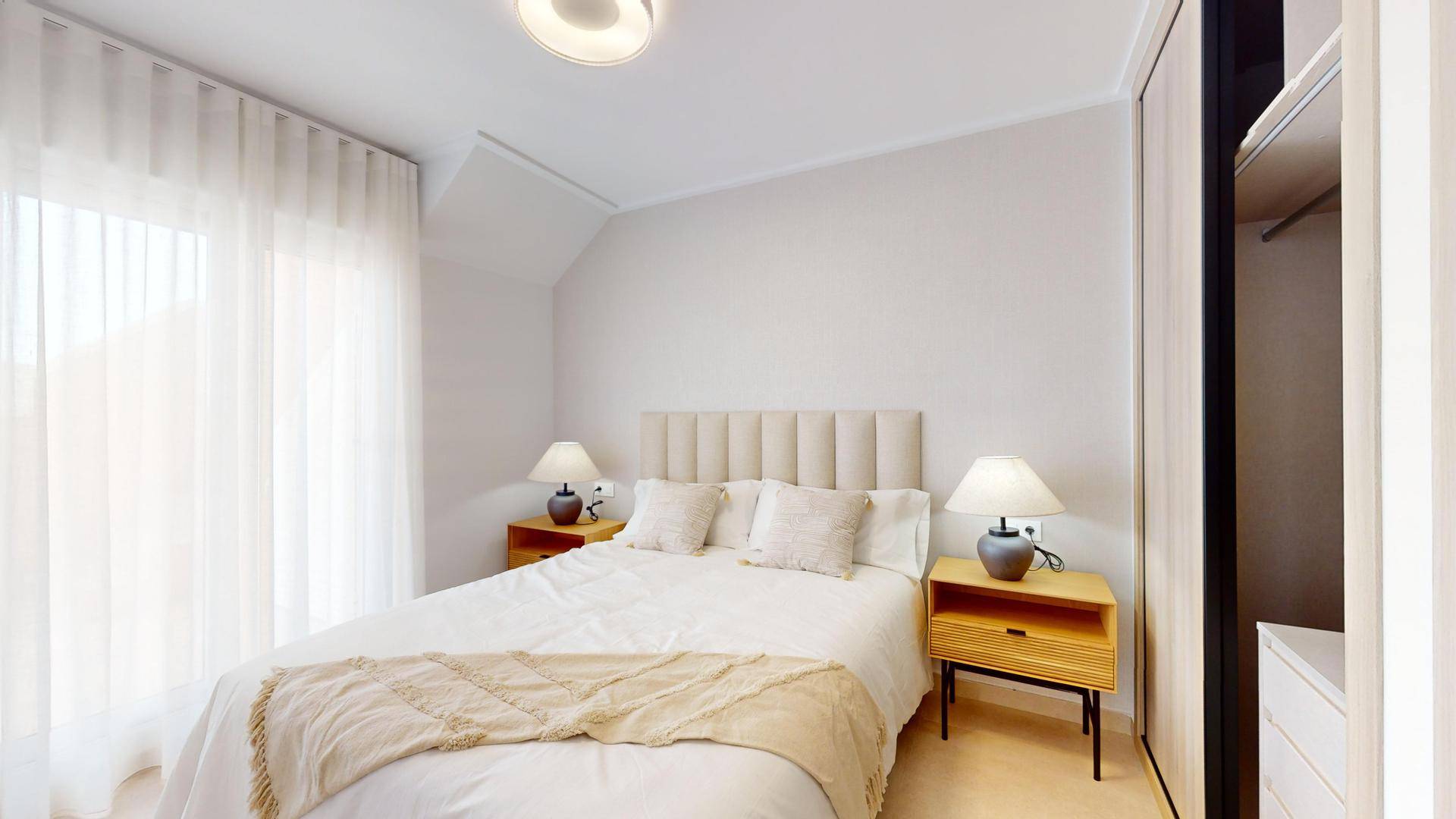 Helles Schlafzimmer mit Doppelbett, gepolstertem Kopfteil und integriertem Kleiderschrank.