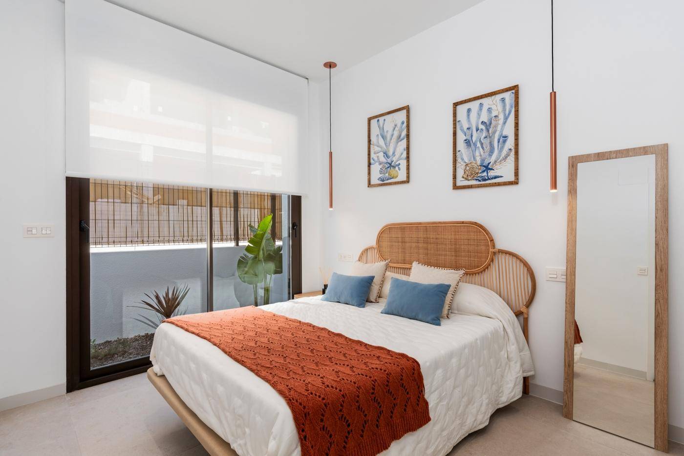 Stilvolles Schlafzimmer mit Rattan-Möbeln, großem Spiegel und Blick auf den Außenbereich.