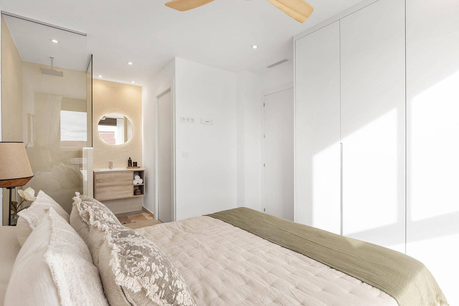 Helles Schlafzimmer mit integriertem Badbereich, Einbauschränken und Deckenventilator.