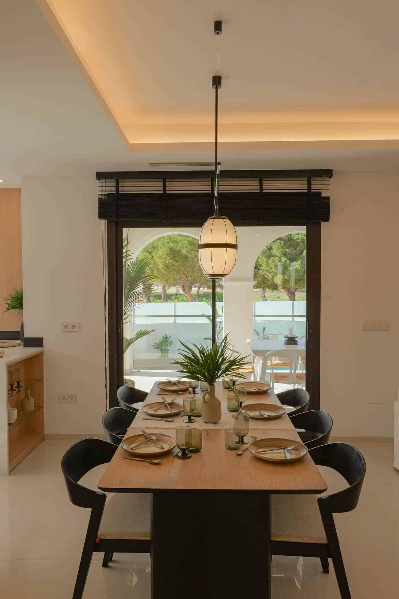 Eleganter Essbereich mit Holztisch und Blick durch große Fenster auf die Terrasse und den Pool.