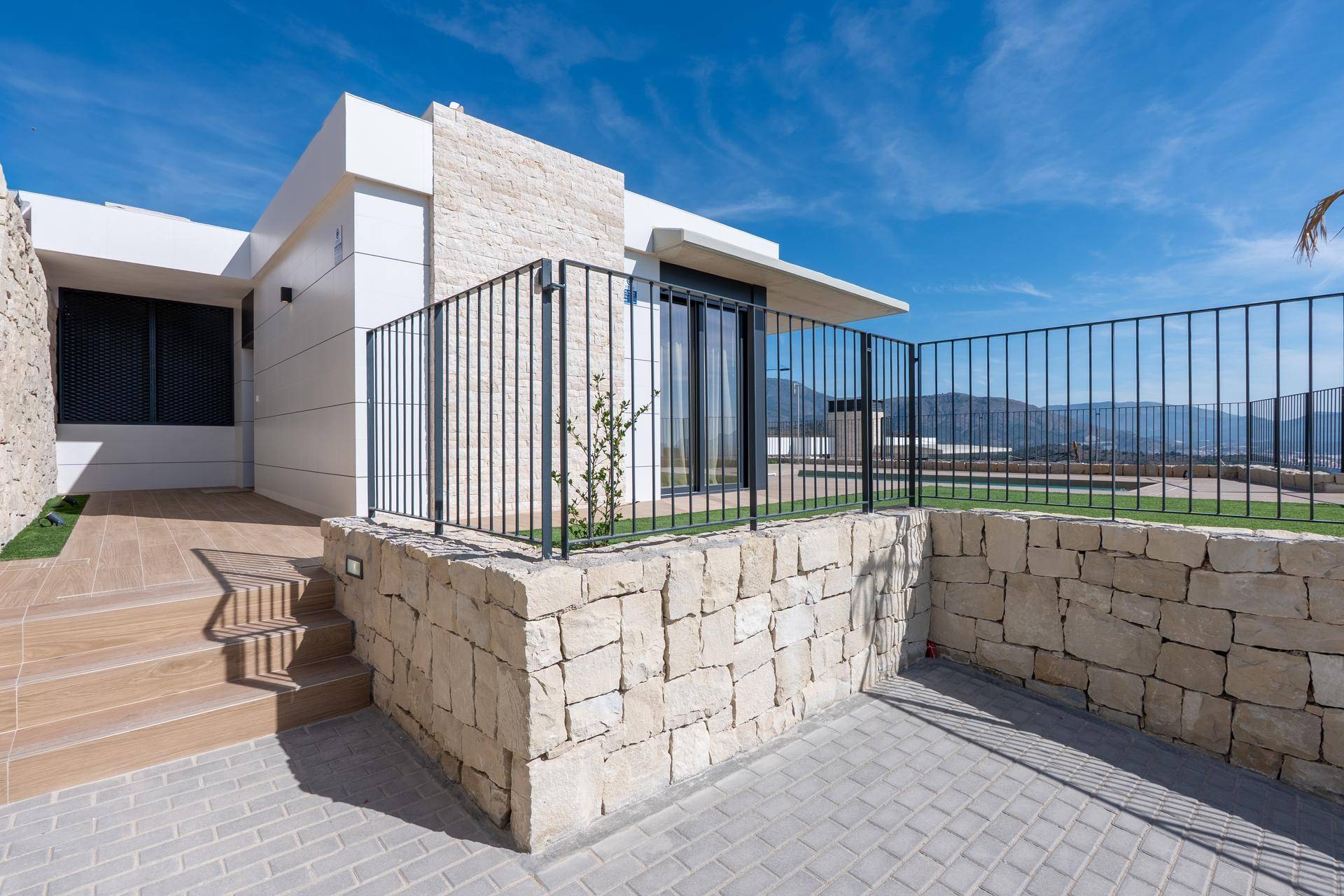 Eingangsbereich einer modernen Villa mit Steinfassade, Treppe und Metallgeländer.
