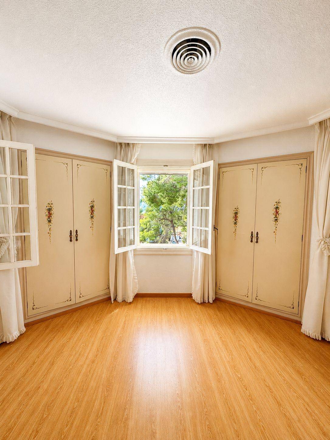Geräumiges Schlafzimmer mit Holzboden und Einbauschränken, die den Raum um das Fenster herum nutzen.