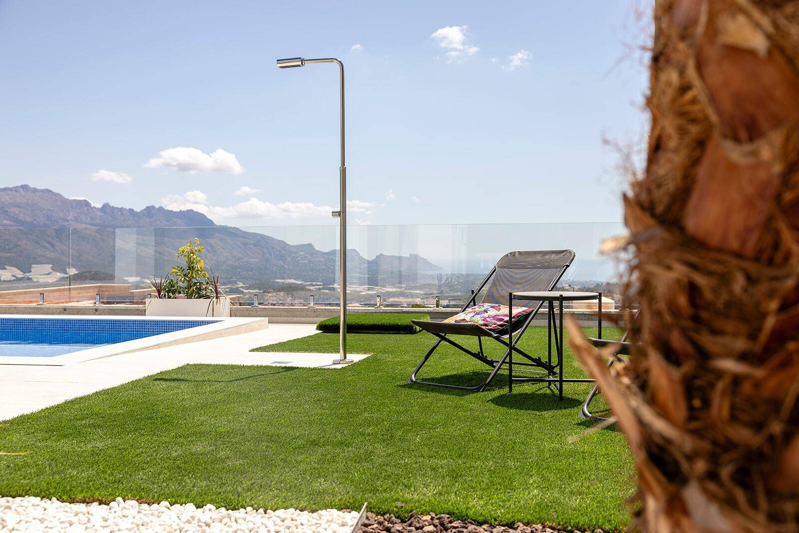 Grüne Rasenfläche neben dem Pool mit Liegestuhl und Blick auf die Berge.