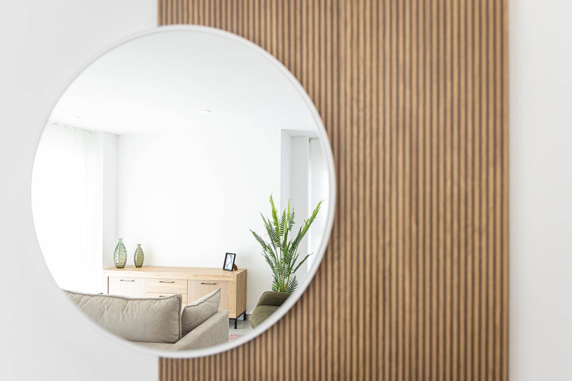 Runder Wandspiegel reflektiert einen Teil des Wohnbereichs mit Pflanze und Sideboard.