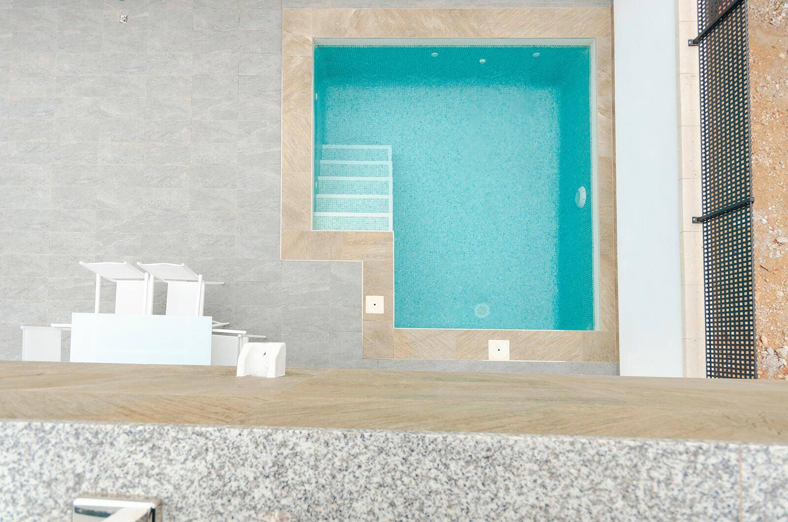 Draufsicht auf den rechteckigen Pool mit Mosaikfliesen und angrenzender Terrasse.