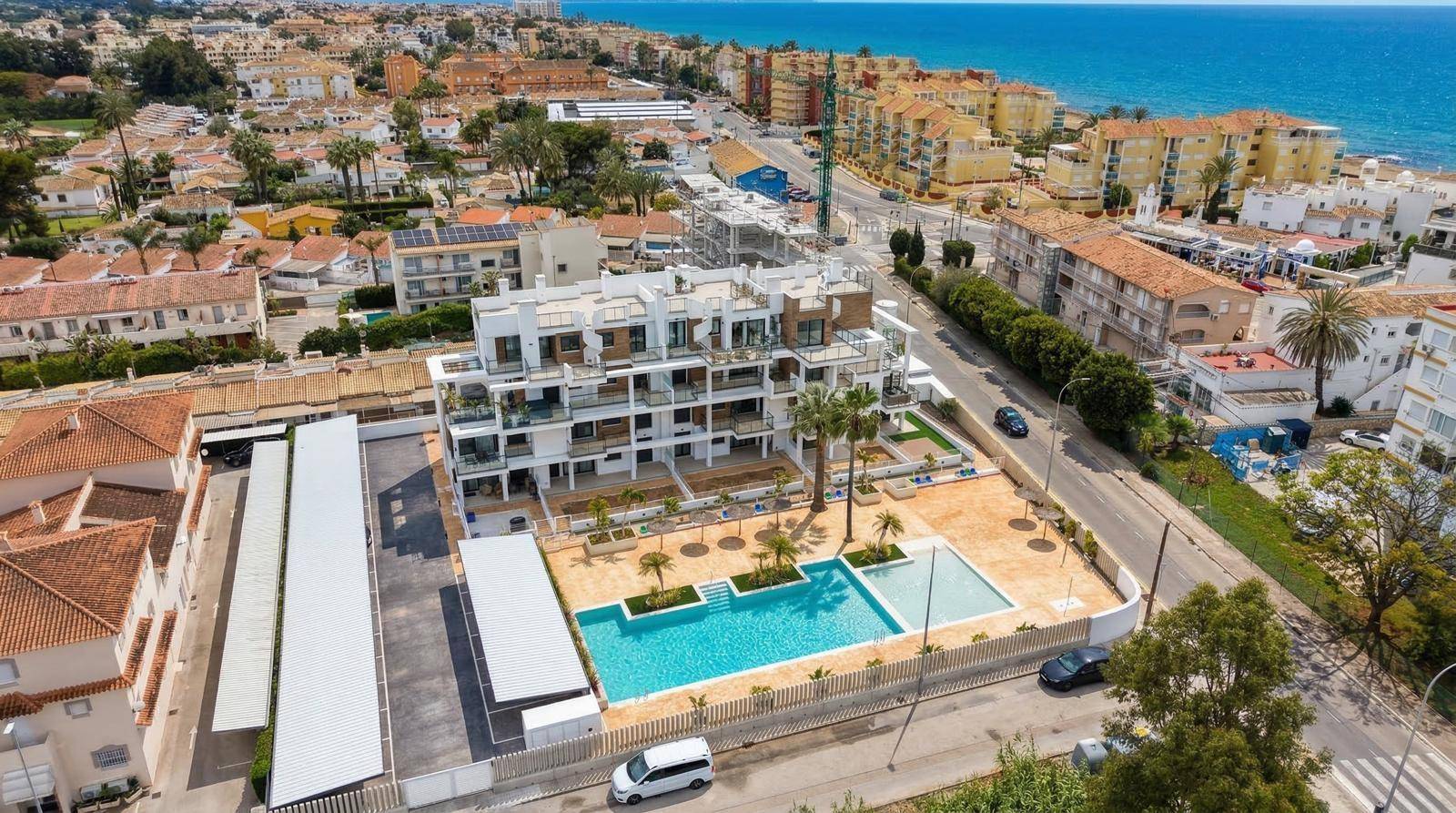 Weitläufige Luftaufnahme eines neuen Apartmentgebäudes mit Pool und Meerblick in Küstennähe.