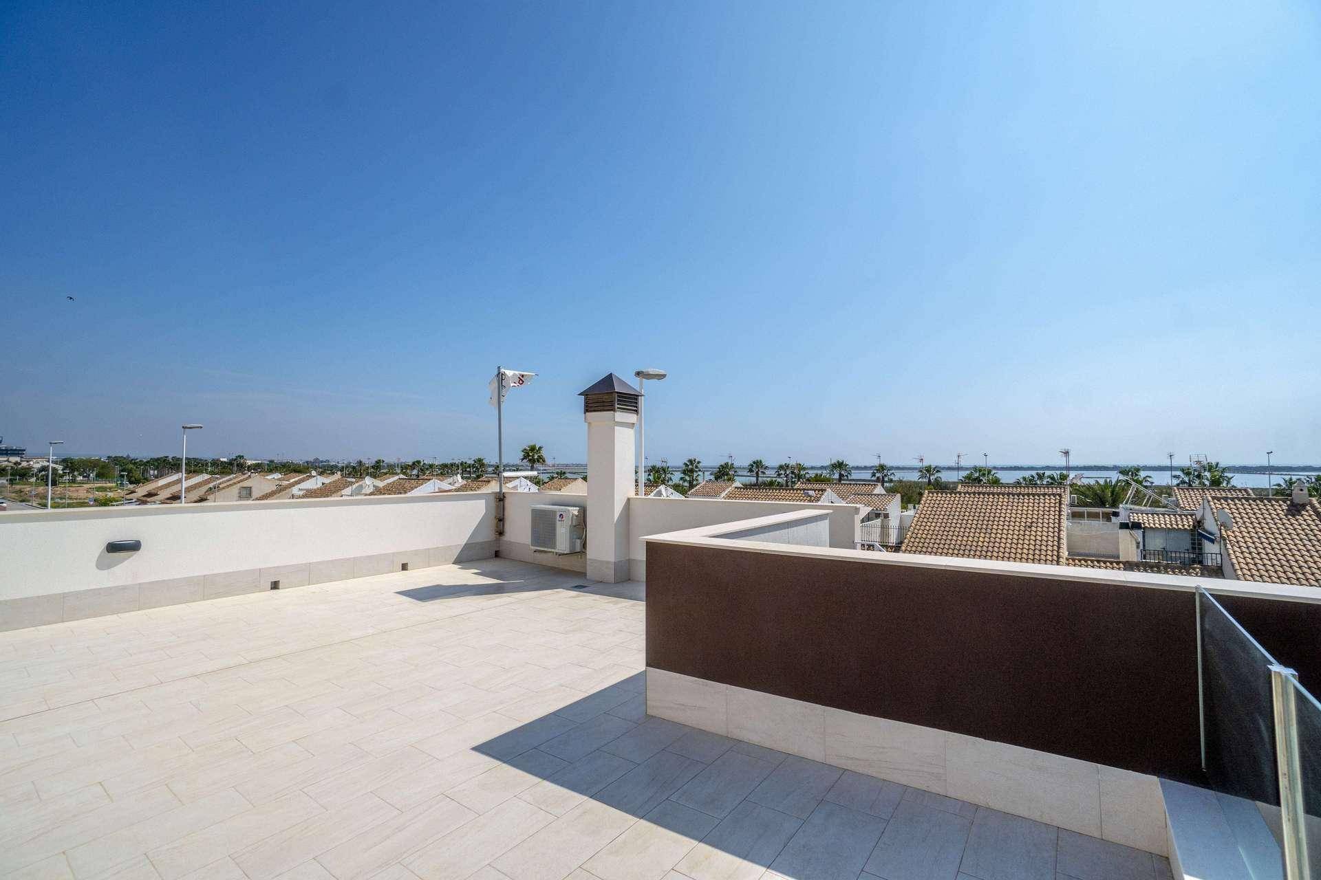 Weitläufige Dachterrasse mit hellen Fliesen, Kamin und Panoramablick auf das Meer in der Ferne.