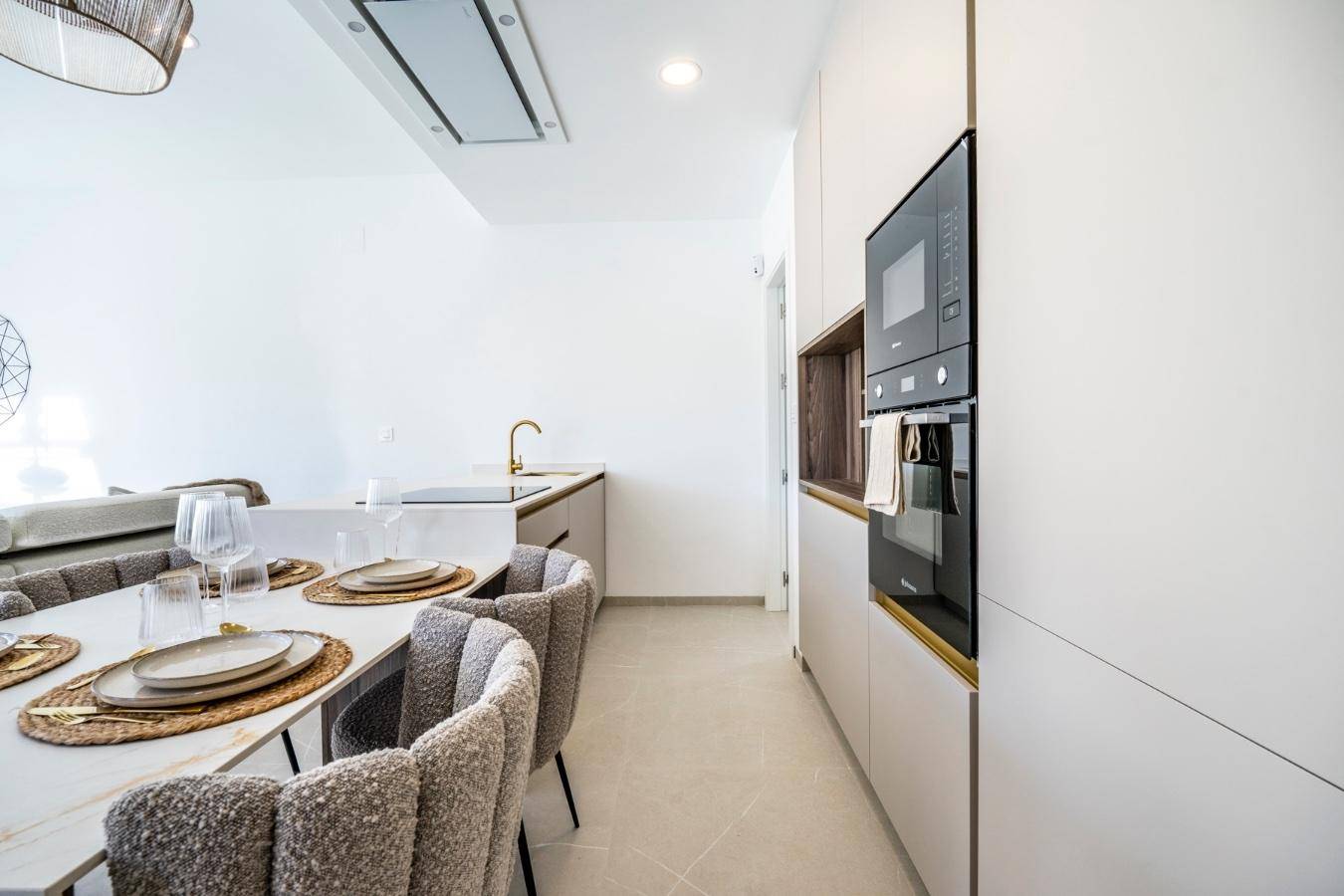 Moderne Küche mit integrierten Geräten, goldenen Armaturen und Essbereich in offenem Wohnkonzept.