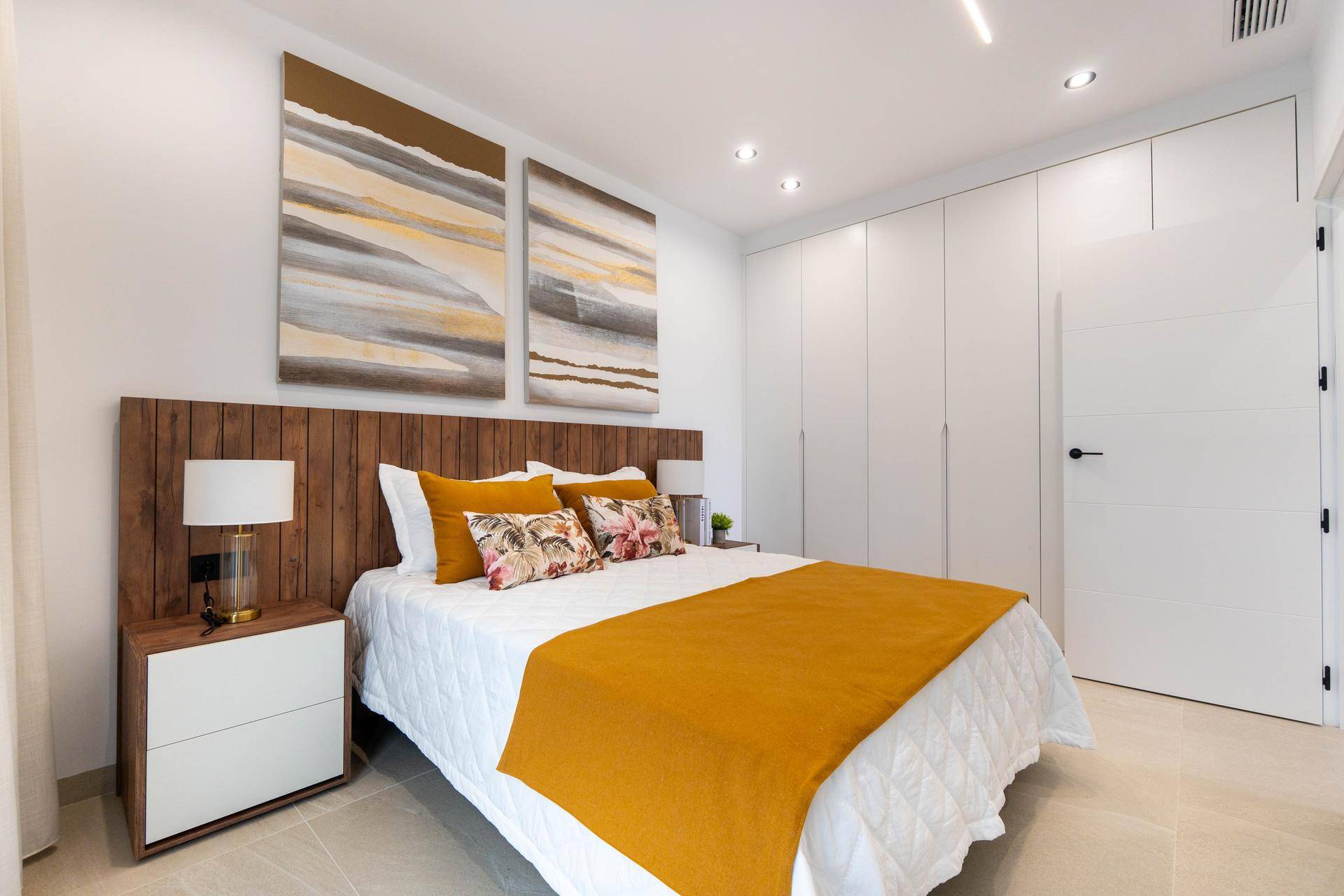 Stilvolles Schlafzimmer mit Holzkopfteil, Einbauschränken und modernen Kunstwerken.