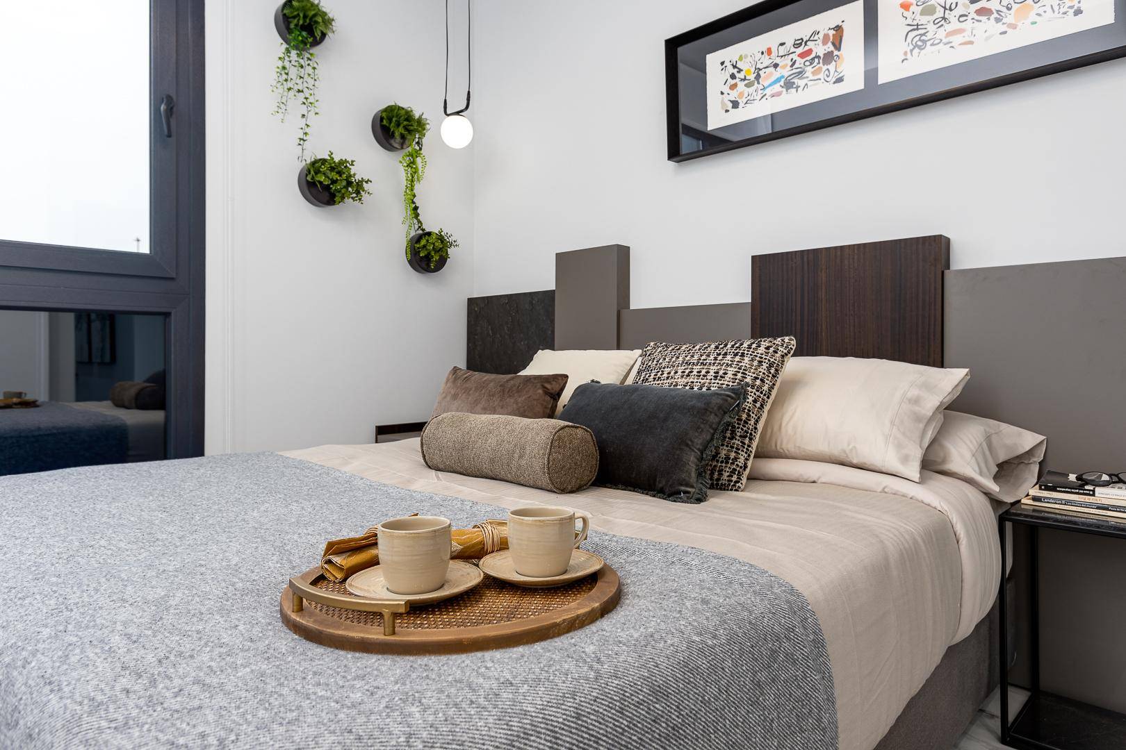 Helles Schlafzimmer mit bequemen Bett, Nachttisch und dekorativen Pflanzen an der Wand.