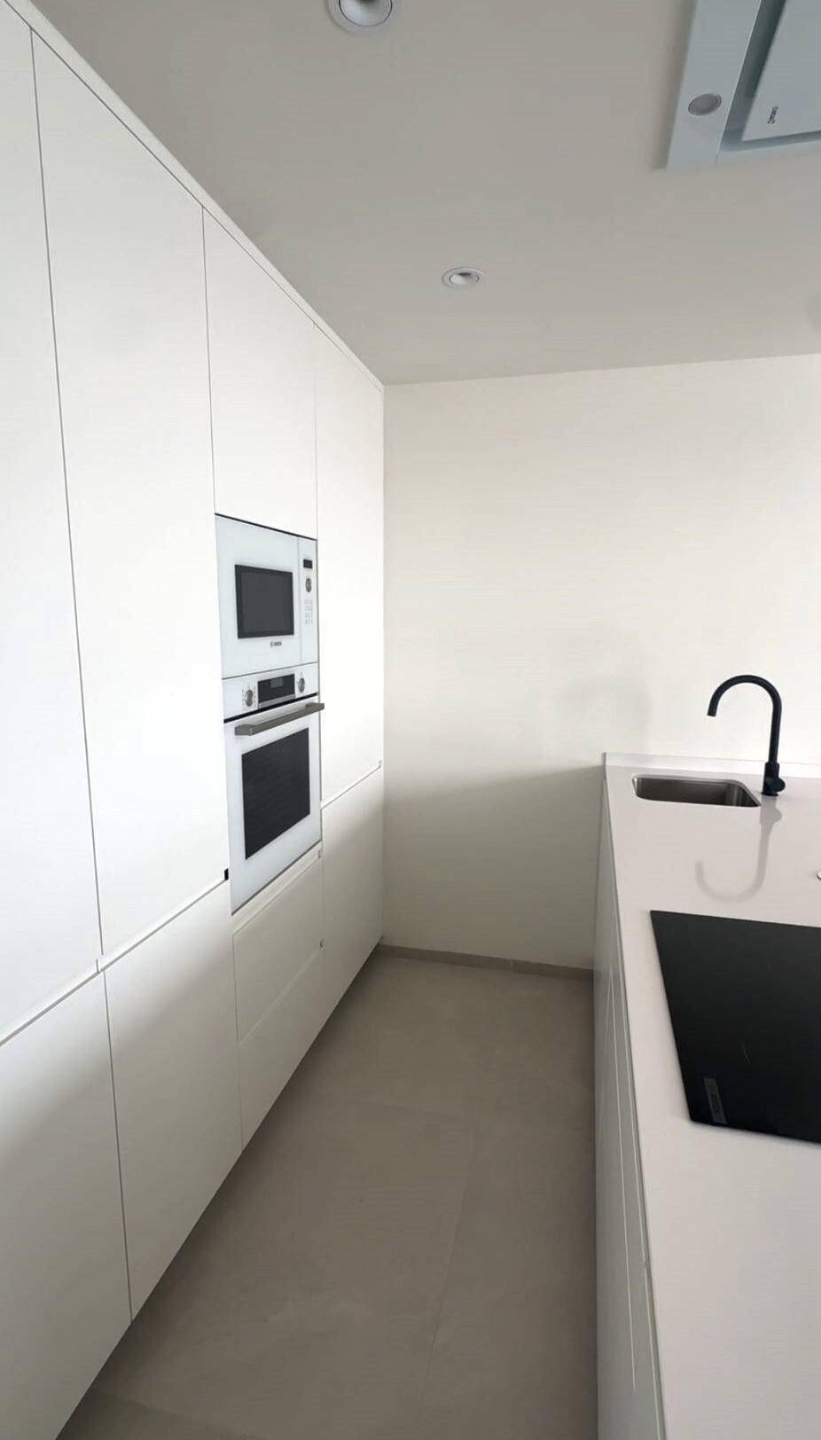 Helle, moderne Küche mit weißen Schränken, integrierten Geräten und Spüle.