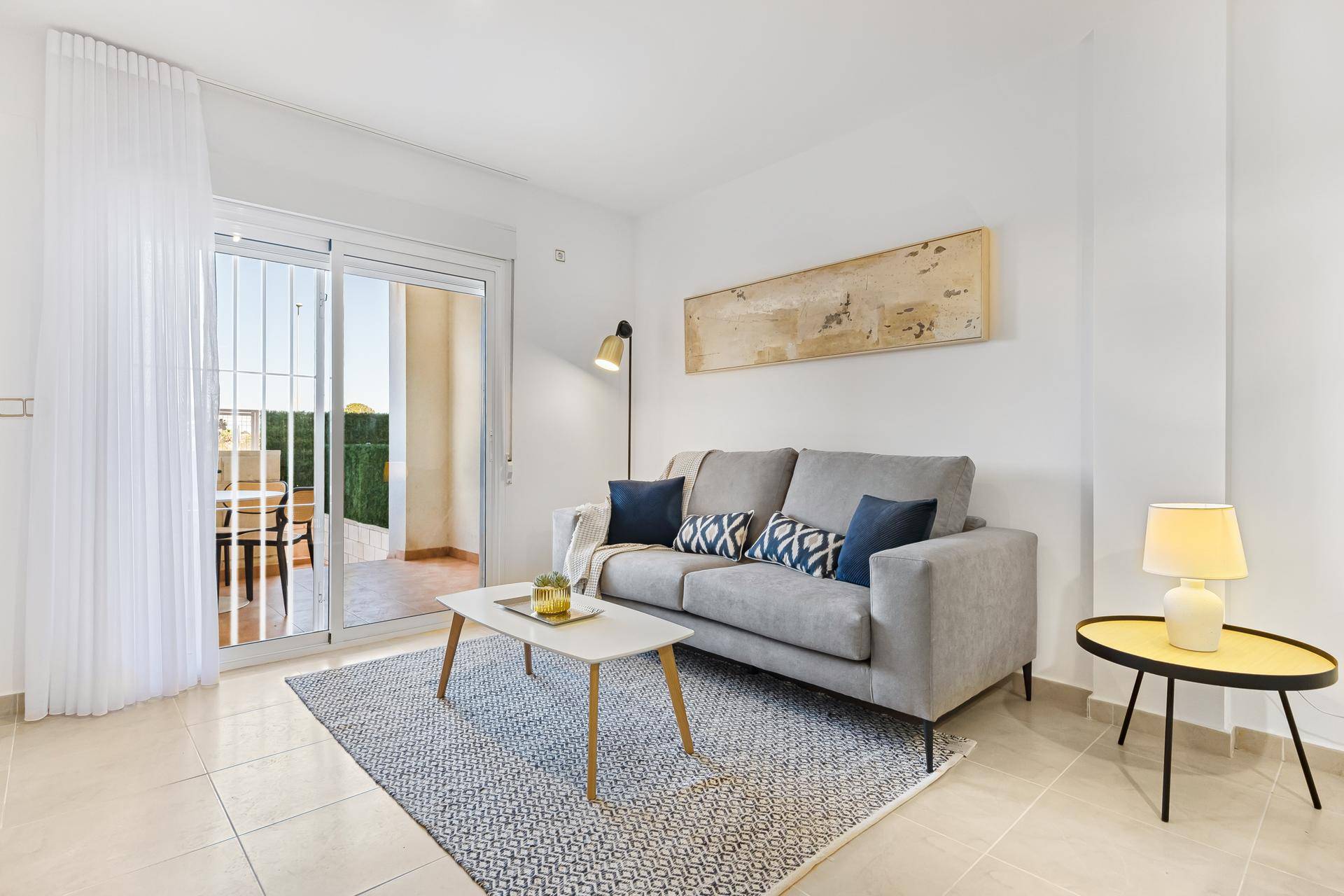 Helles Wohnzimmer mit grauem Sofa, Couchtisch und Zugang zu einem Außenbereich.