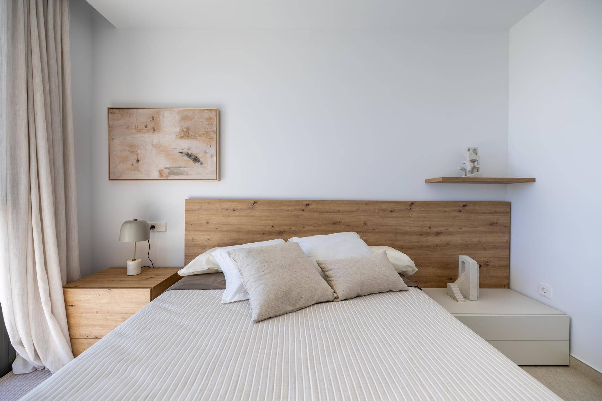 Ruhiges Schlafzimmer mit Doppelbett, Holzkopfteil und minimalistischer Einrichtung.