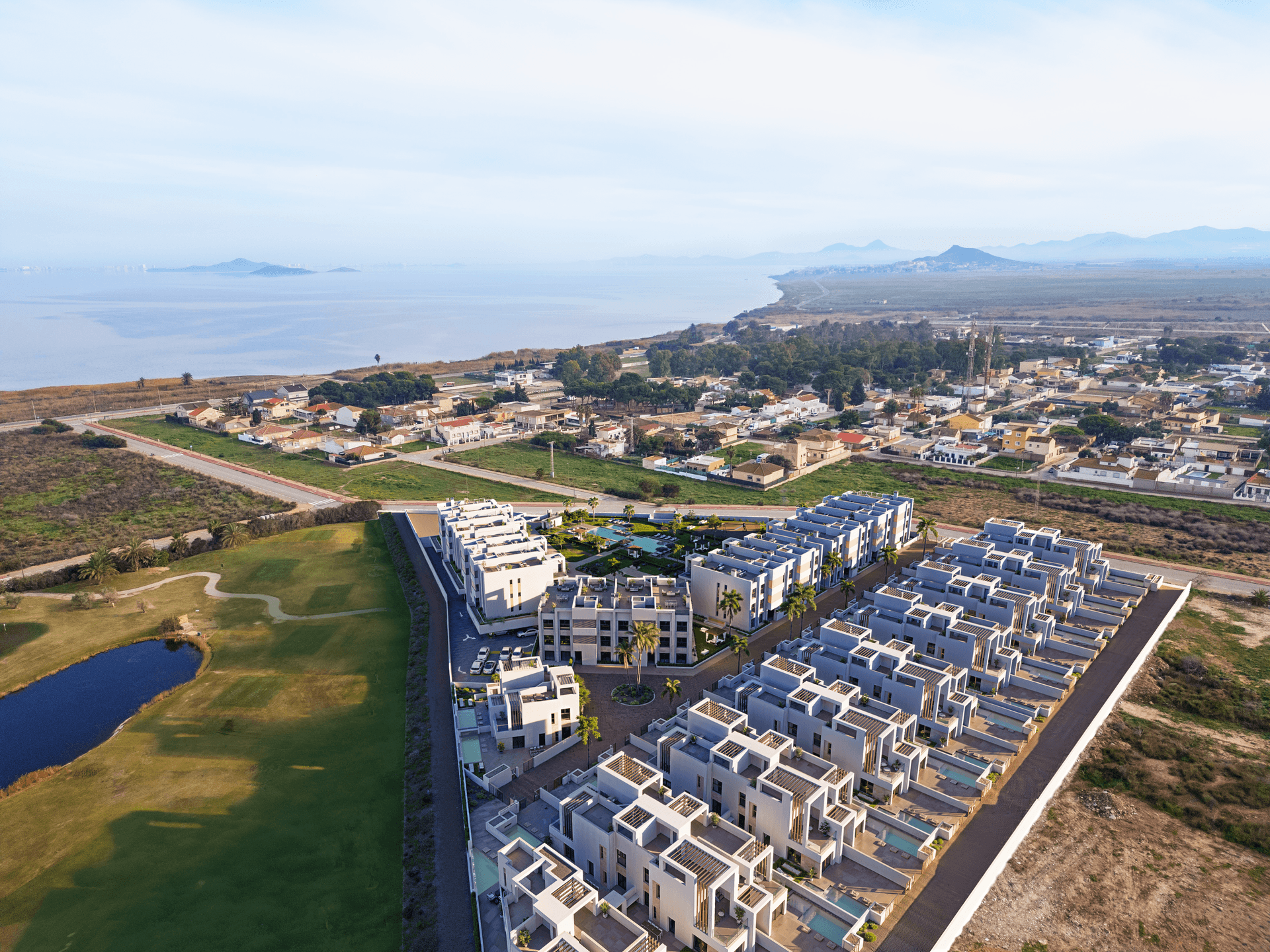 Luftaufnahme einer modernen Wohnanlage mit Meerblick, umgeben von Natur und Golfplätzen.