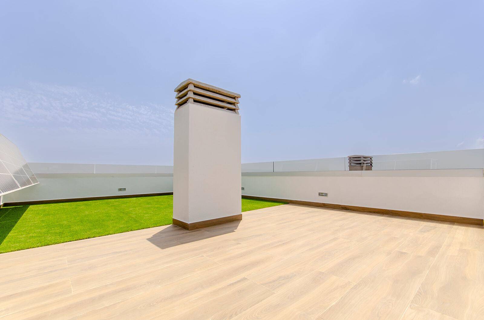Helle Dachterrasse mit Kunstrasen, Kamin und weitem Blick unter blauem Himmel.