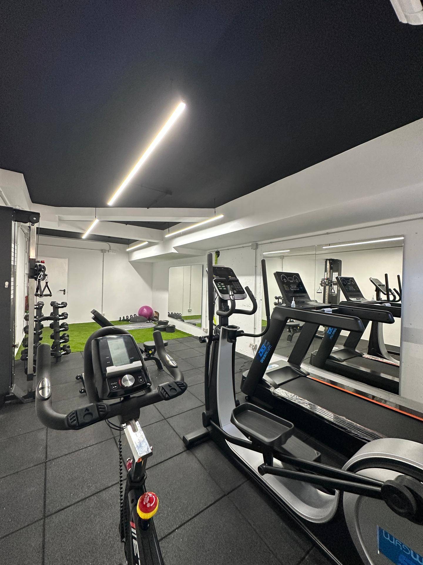 Gut ausgestatteter Fitnessraum mit Laufband, Fahrrad und Hanteln.