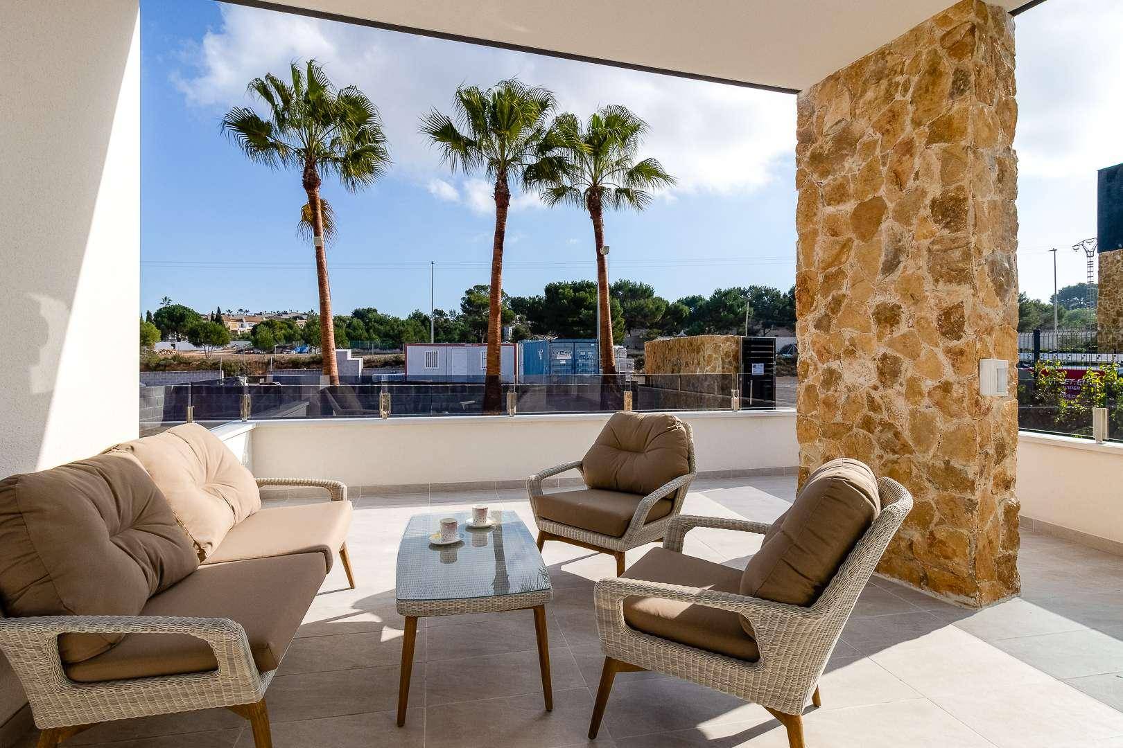 Heller Balkon mit bequemen Loungemöbeln und Blick auf die Umgebung mit Palmen und blauem Himmel.