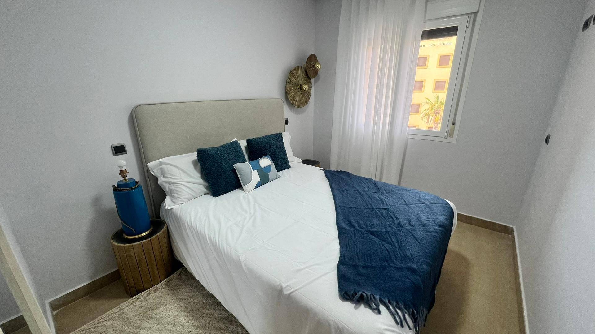 Gemütliches Schlafzimmer mit Doppelbett, blauer Tagesdecke und Fenster für natürliches Licht.