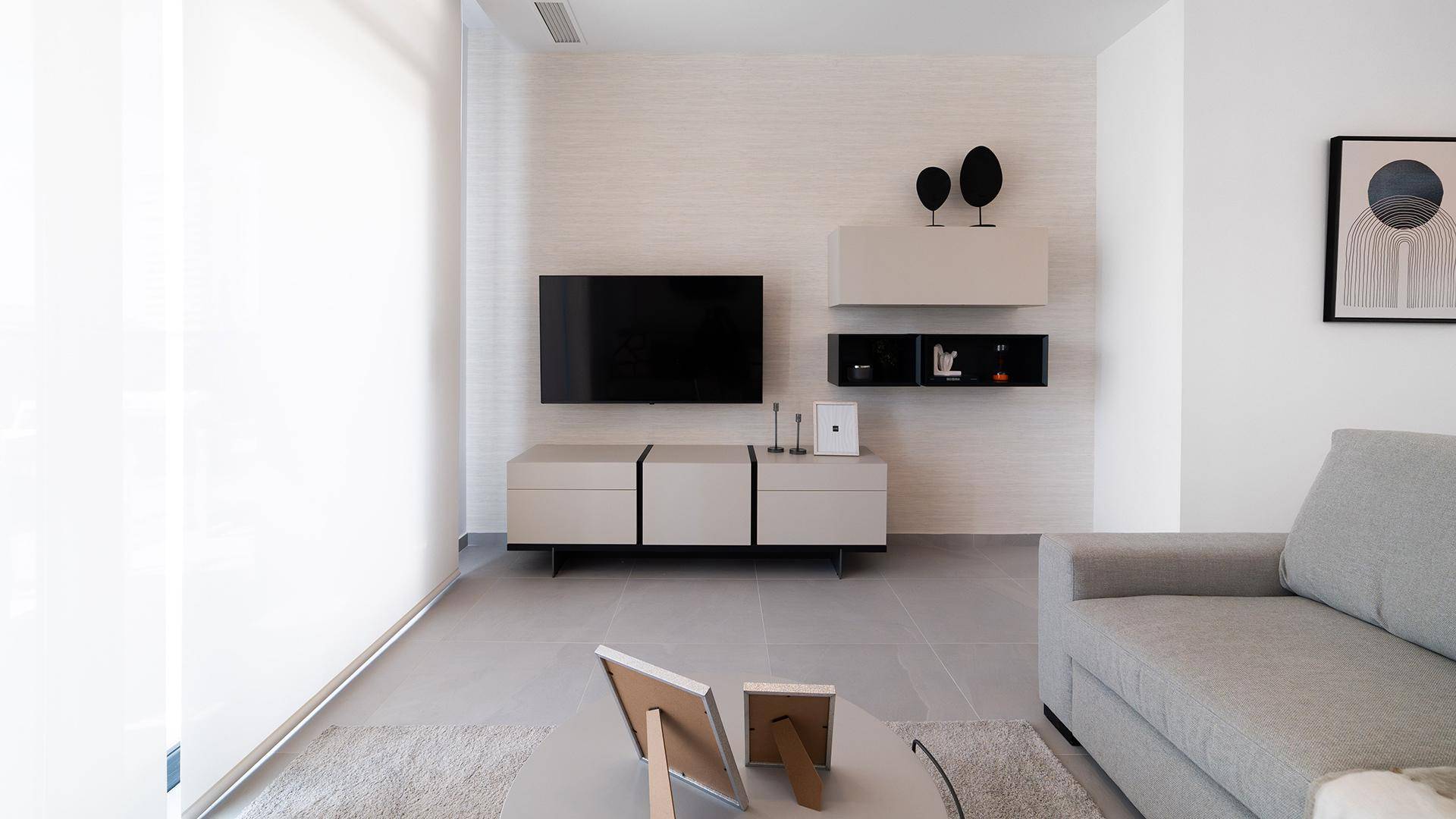 Modernes Wohnzimmer mit beigem Sofa, TV-Möbeln und großen Fenstern.