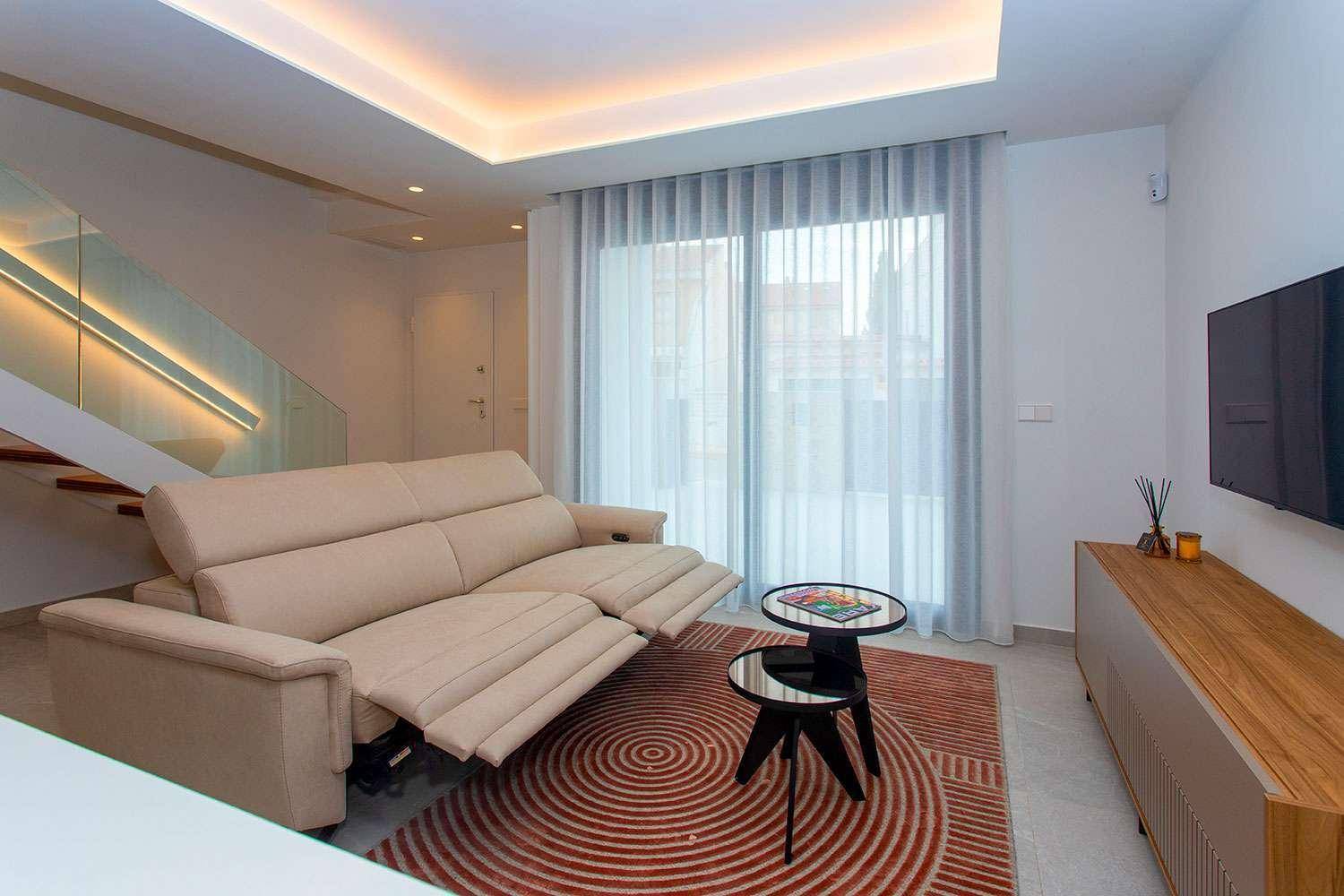 Modernes Wohnzimmer mit beigem Sofa, indirekter Beleuchtung und großen Fenstern für viel Tageslicht.