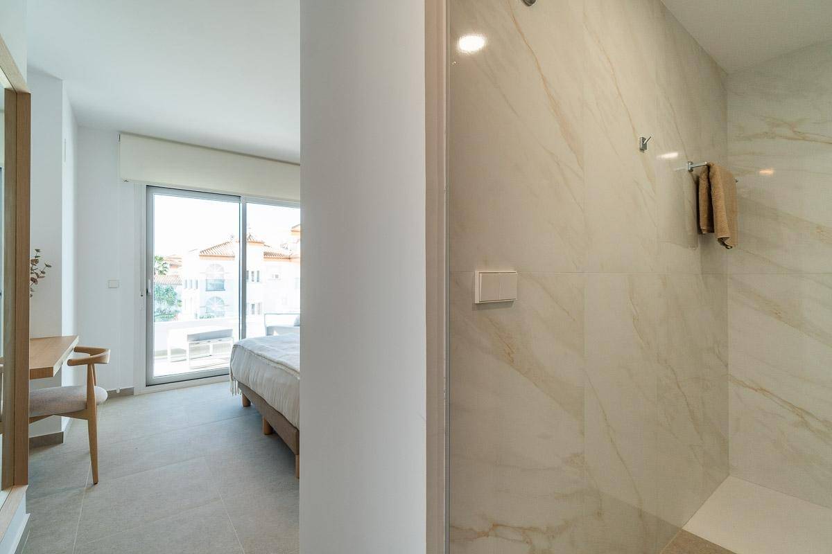 Modernes Badezimmer mit eleganten Marmorfliesen und ebenerdiger Dusche, vom Flur aus sichtbar.