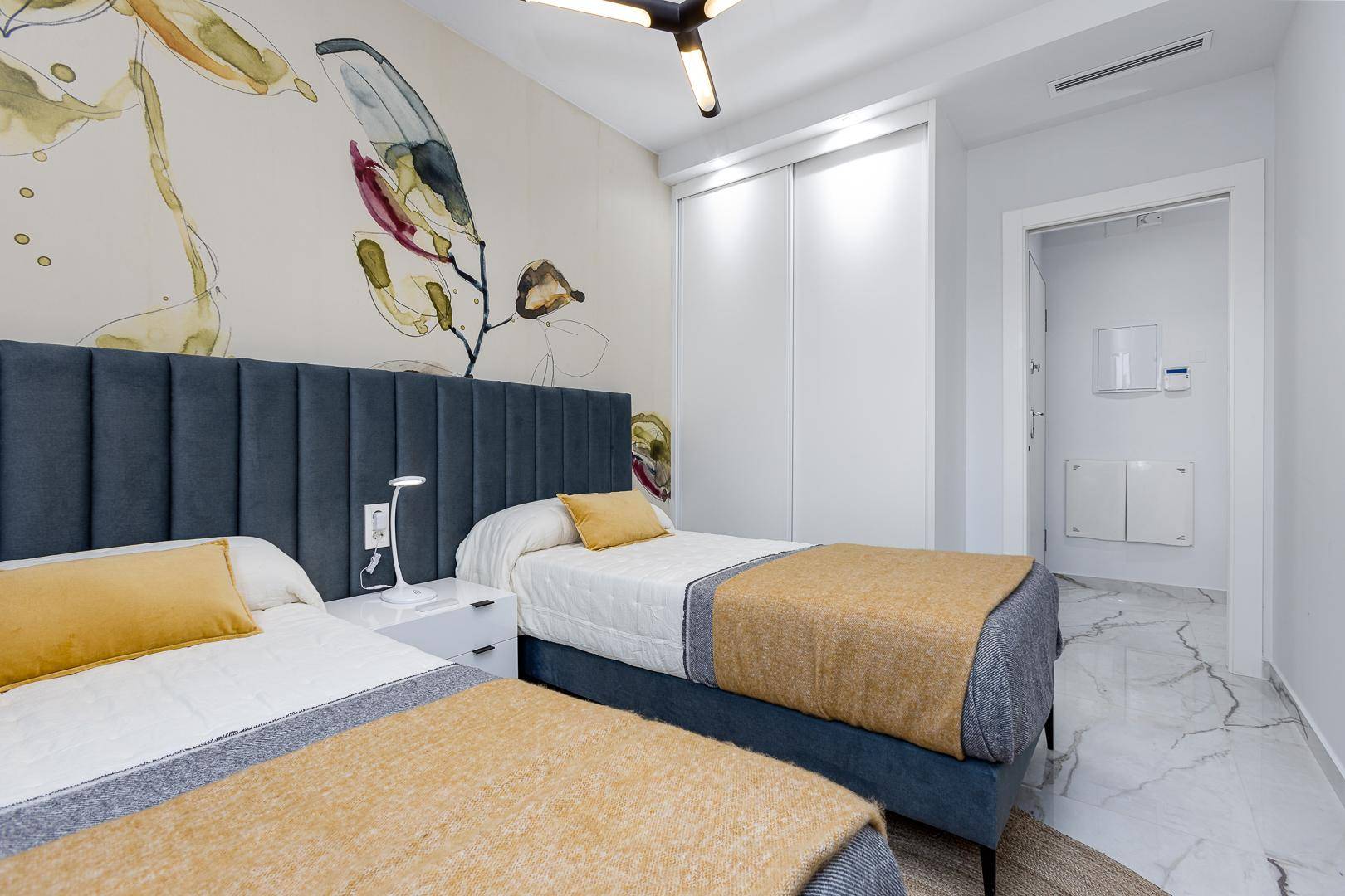 Helles Schlafzimmer mit zwei Einzelbetten, moderner Wanddekoration und Zugang zu einem Nebenraum.
