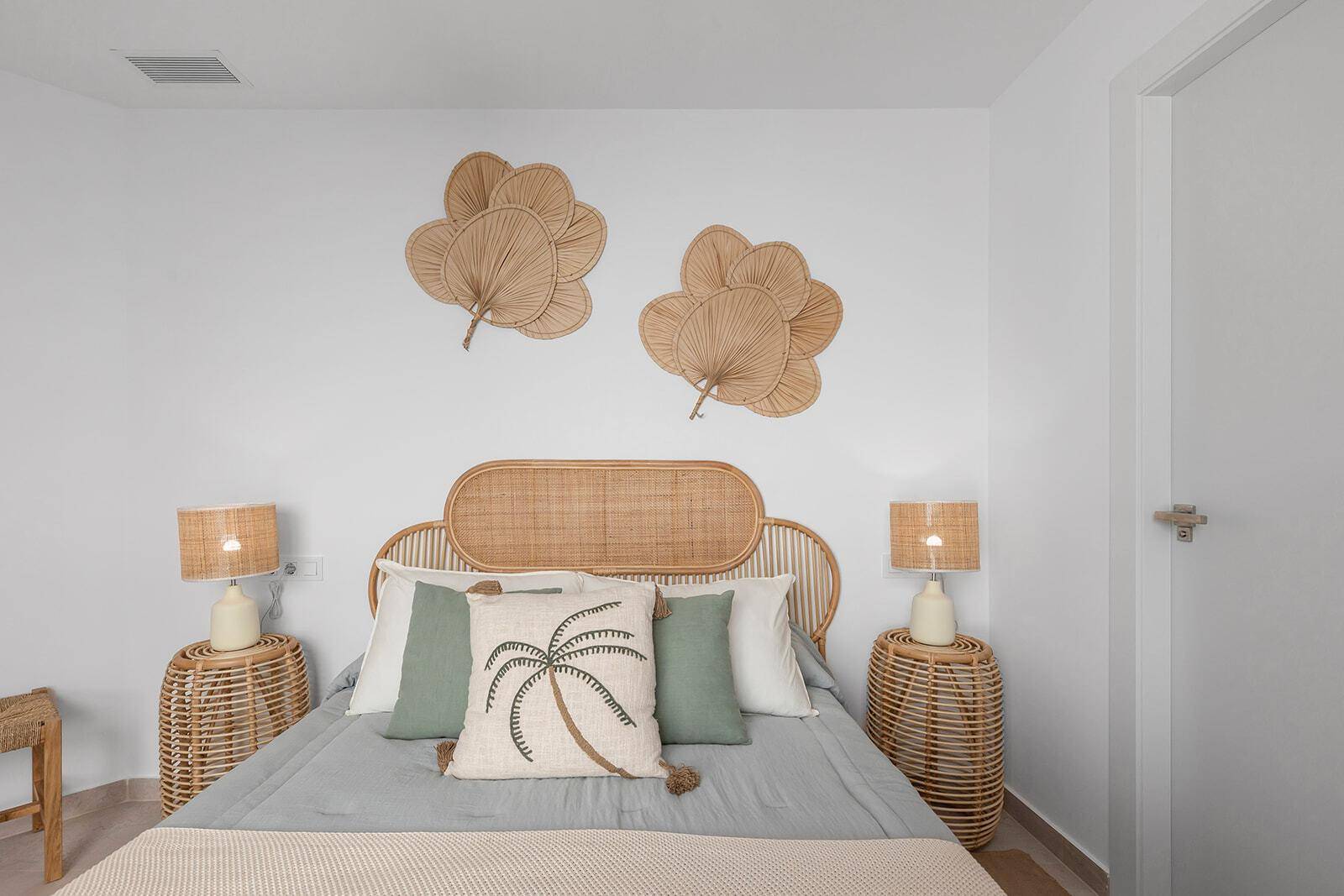 Schlafzimmer mit Rattan-Kopfteil, passenden Nachttischen und tropischen Kissen, die eine gemütliche Atmosphäre schaffen.
