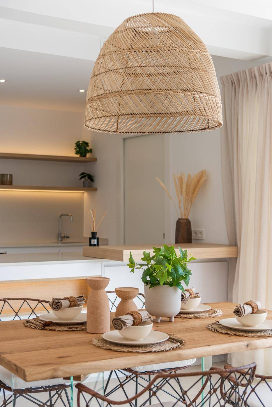 Essbereich mit Holztisch, Rattan-Pendelleuchte und Blick auf die offene Küche.