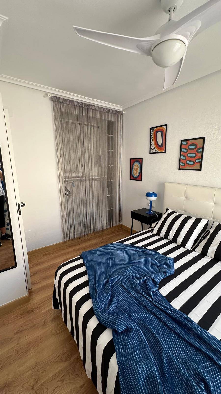 Schlafzimmer mit gestreifter Bettwäsche, Holzboden und Zugang zu einem kleinen Balkon.