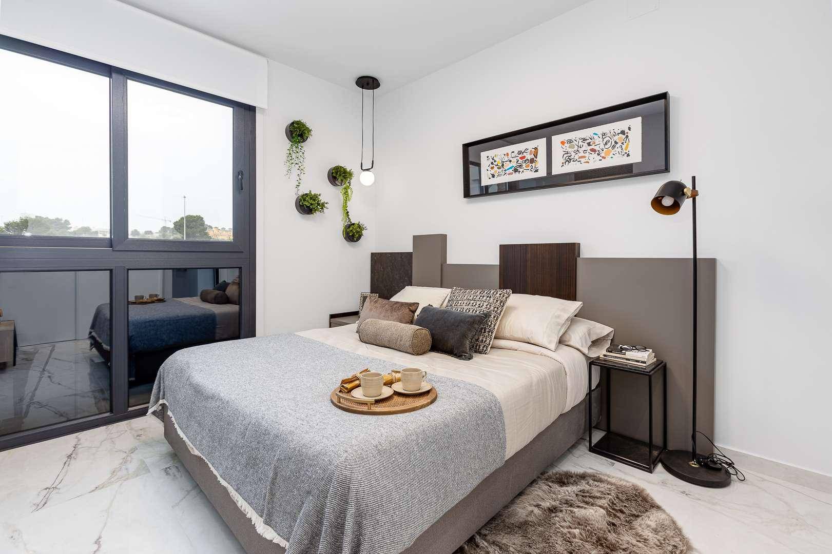 Helles Schlafzimmer mit großem Fenster, bequemen Bett und moderner Wanddekoration mit Pflanzen.
