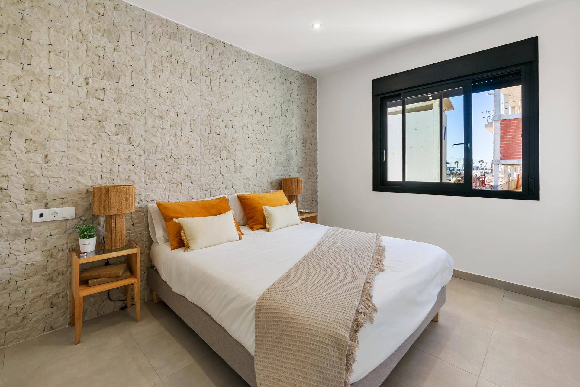 Helles Schlafzimmer mit strukturierter Steinwand, großem Fenster und modernen Nachttischen.