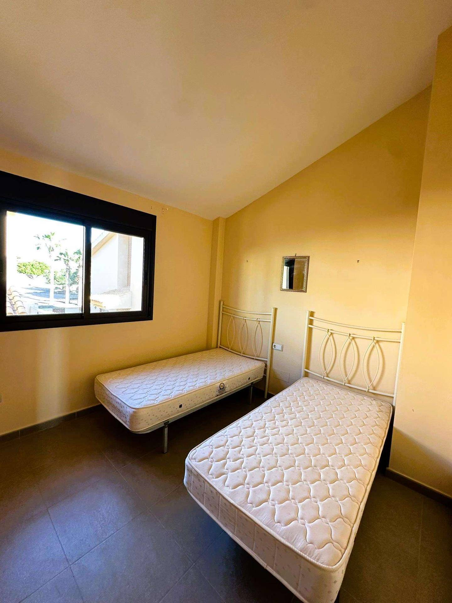 Schlafzimmer mit zwei Einzelbetten, Fliesenboden und einem Fenster mit Blick nach draußen.