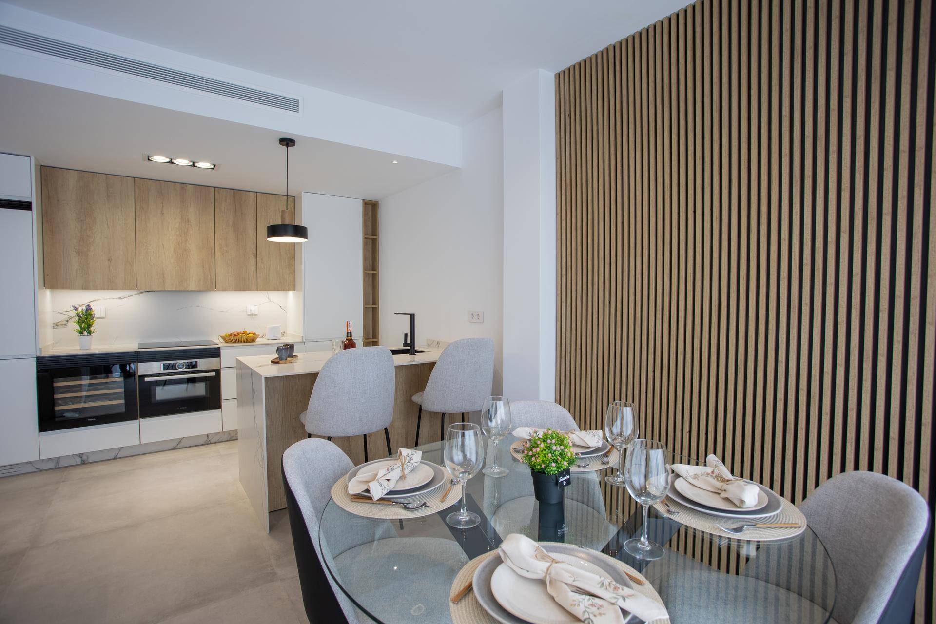 Eleganter Essbereich mit rundem Glastisch, modernen Stühlen und dekorativer Holzlamellenwand.