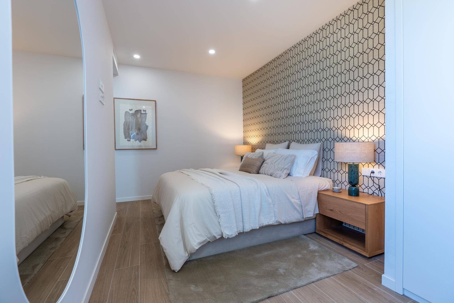 Schlafzimmer mit Doppelbett, geometrischer Tapete und großem Spiegel, der den Raum erweitert.