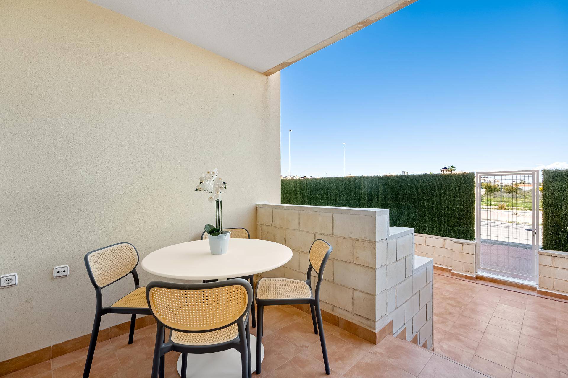 Sonniger Terrassenbereich mit Sitzgelegenheiten und Zugang zu einem umzäunten Außenbereich.