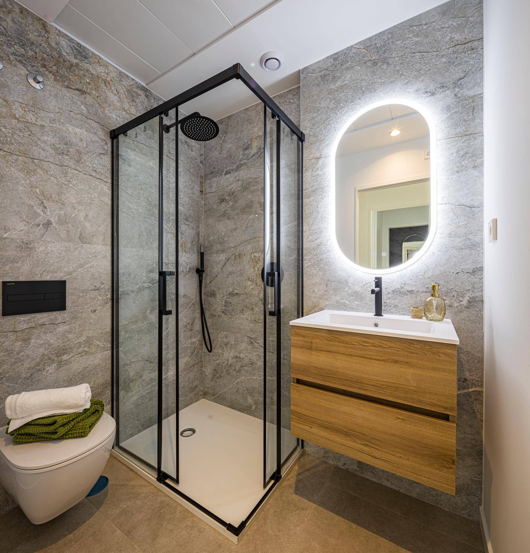 Modernes Badezimmer mit begehbarer Dusche, schwebendem Waschtisch und beleuchtetem Spiegel.