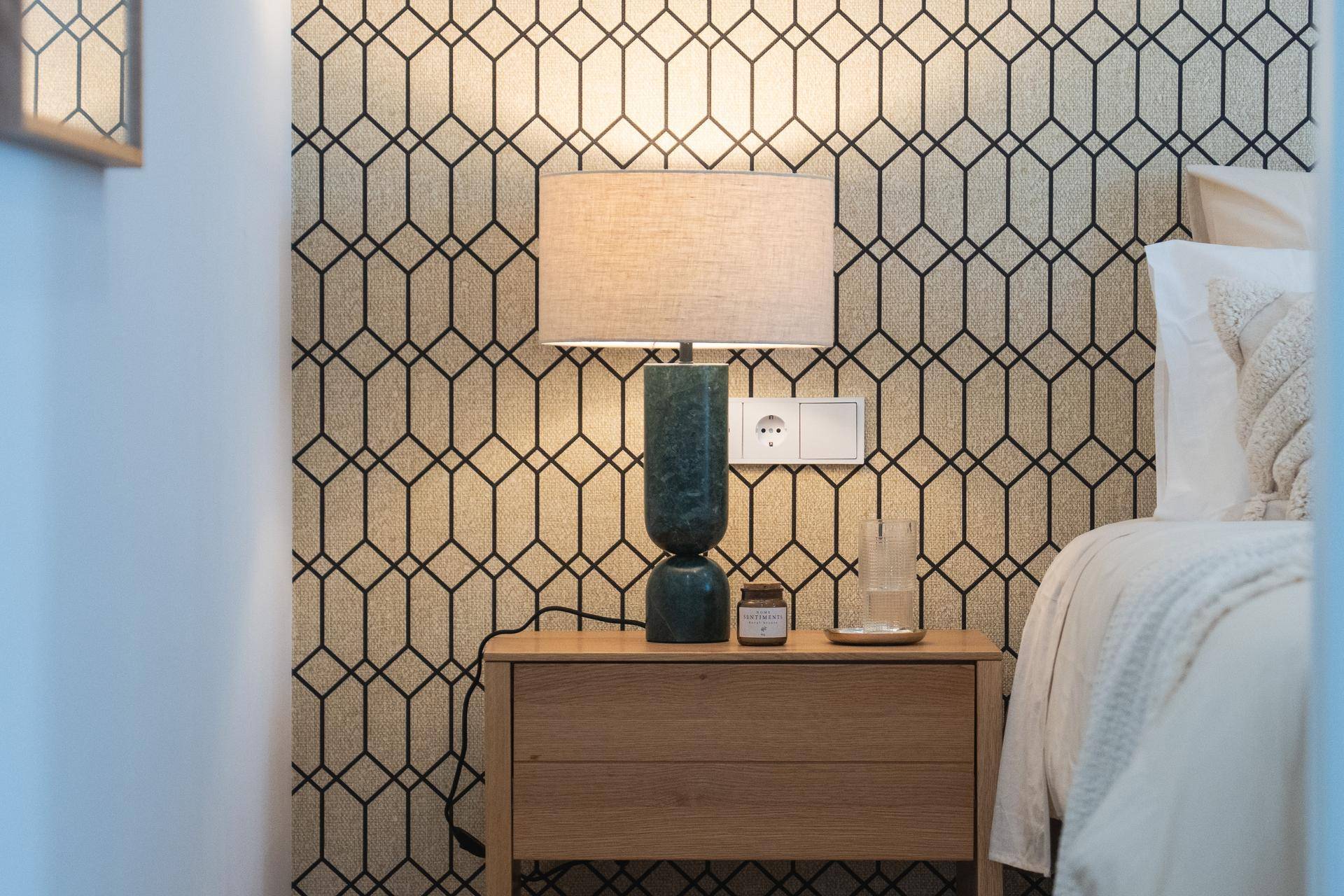 Detailansicht eines Nachttisches mit moderner Lampe vor einer stilvollen geometrischen Tapete.
